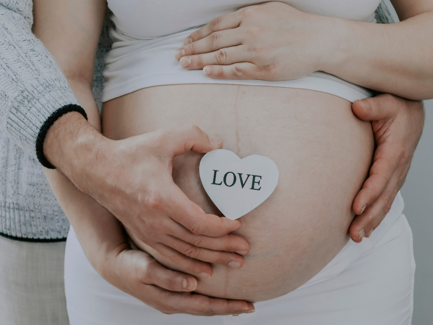Man Holds a Heart and Belly of Pregnant Woman